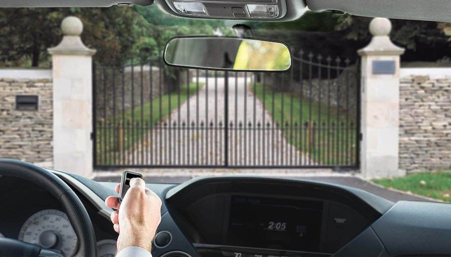 Person inside their car clicking a gate remote in front of a driveway gate so it will open 